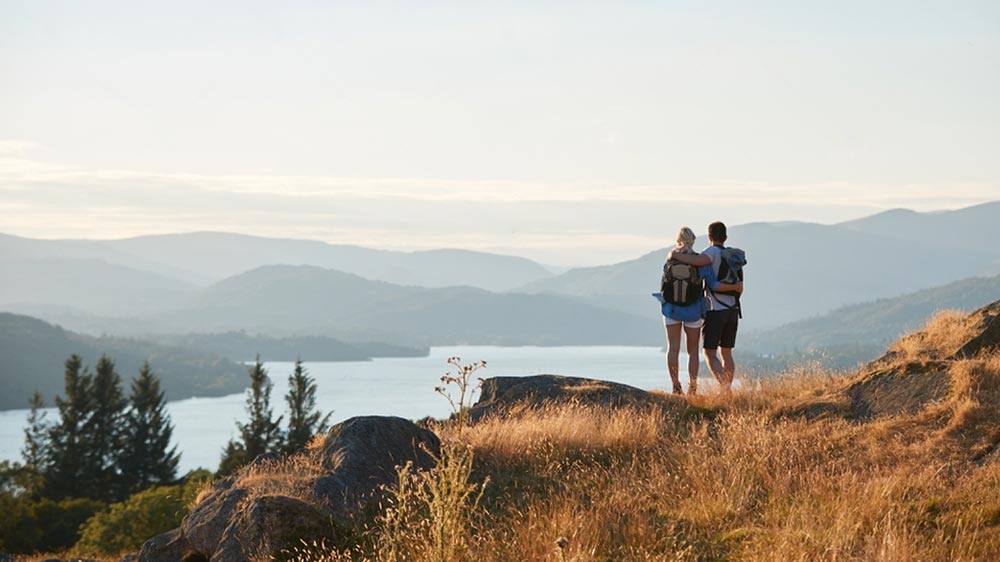 un couple de dos en haut d'une montage et face à un lac entouré de montagne