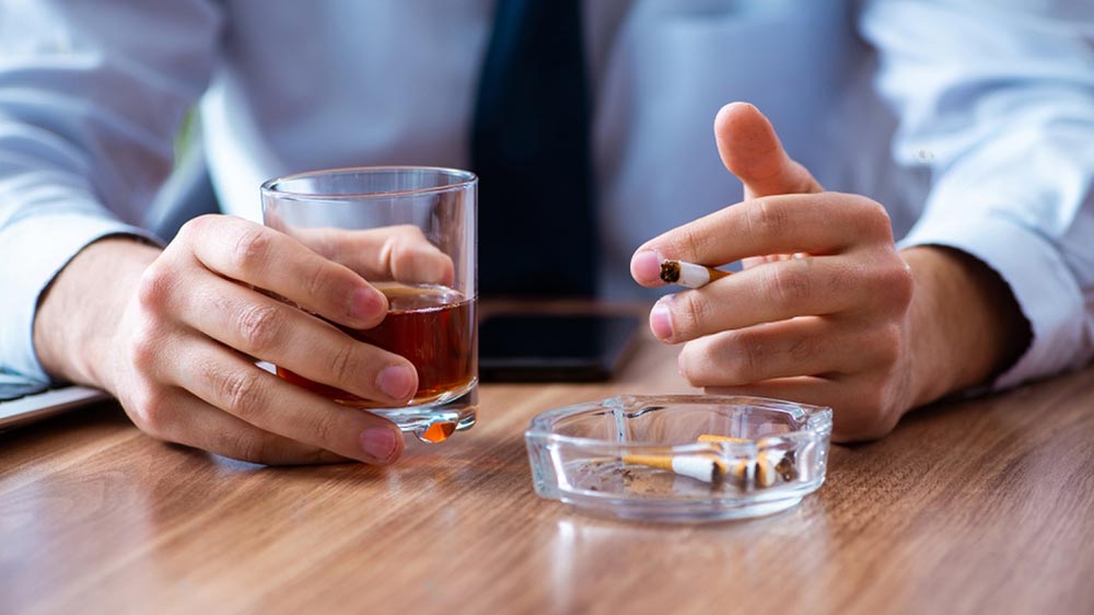 un homme boit un verre de whisky et fume une cigarette 