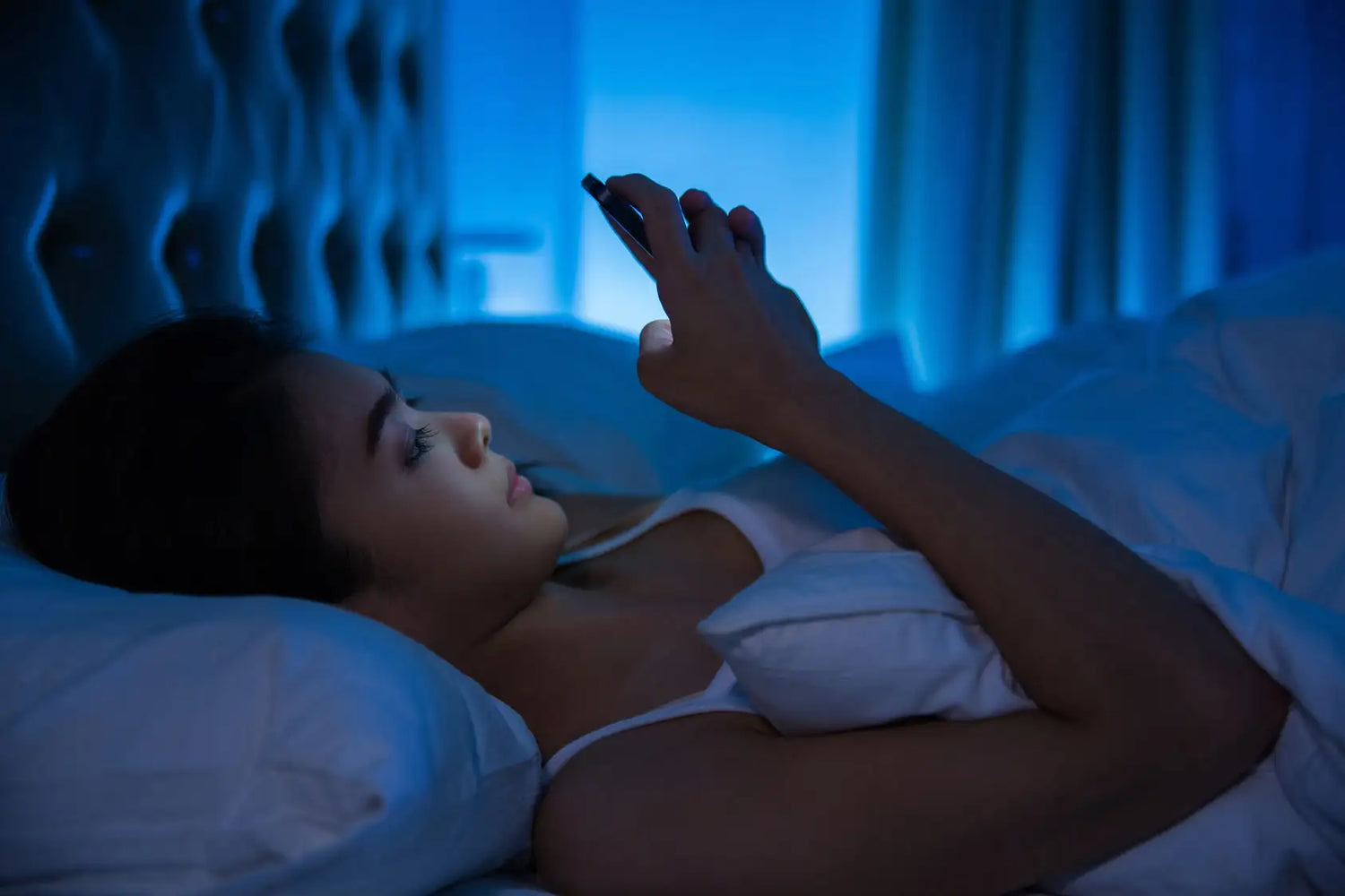 une femme regarde son smartphone dans le lit